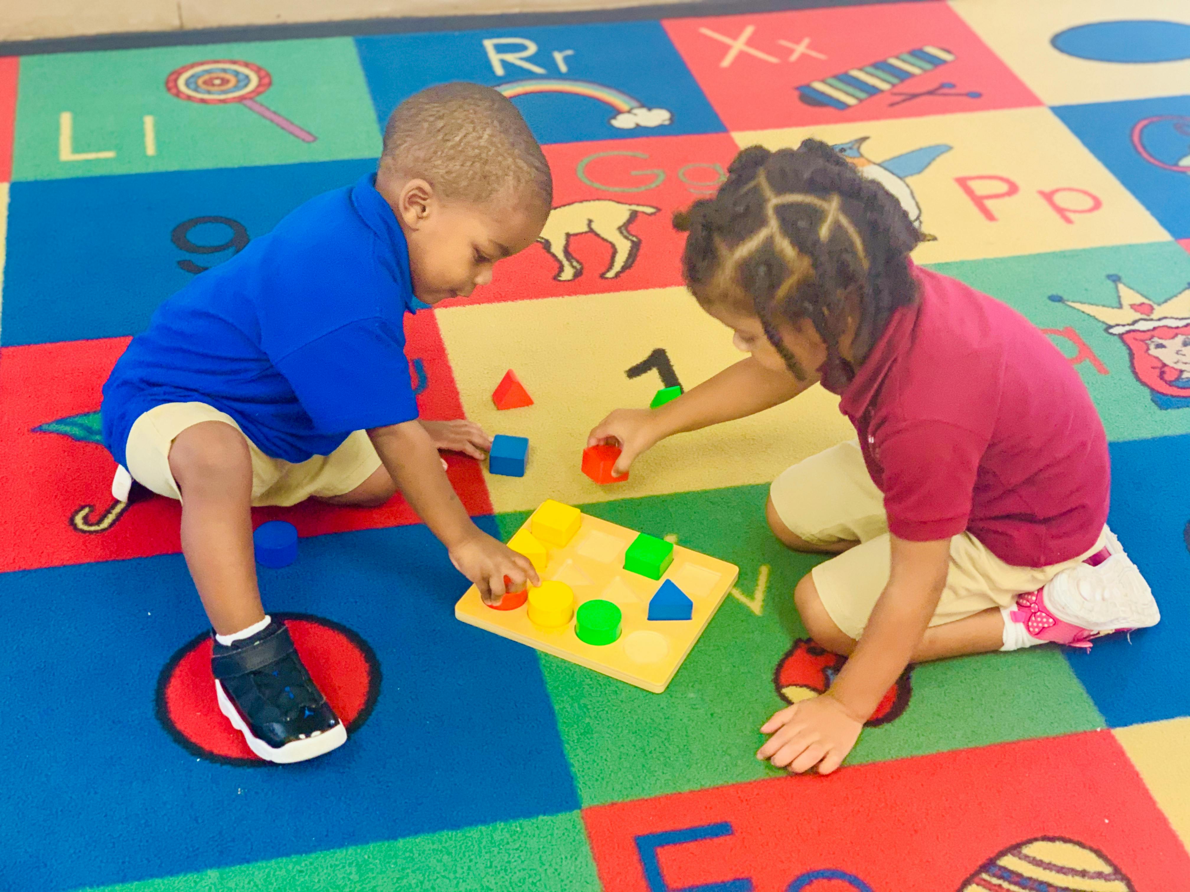 Two children playing with shape sorter toys on a colorful alphabet rug