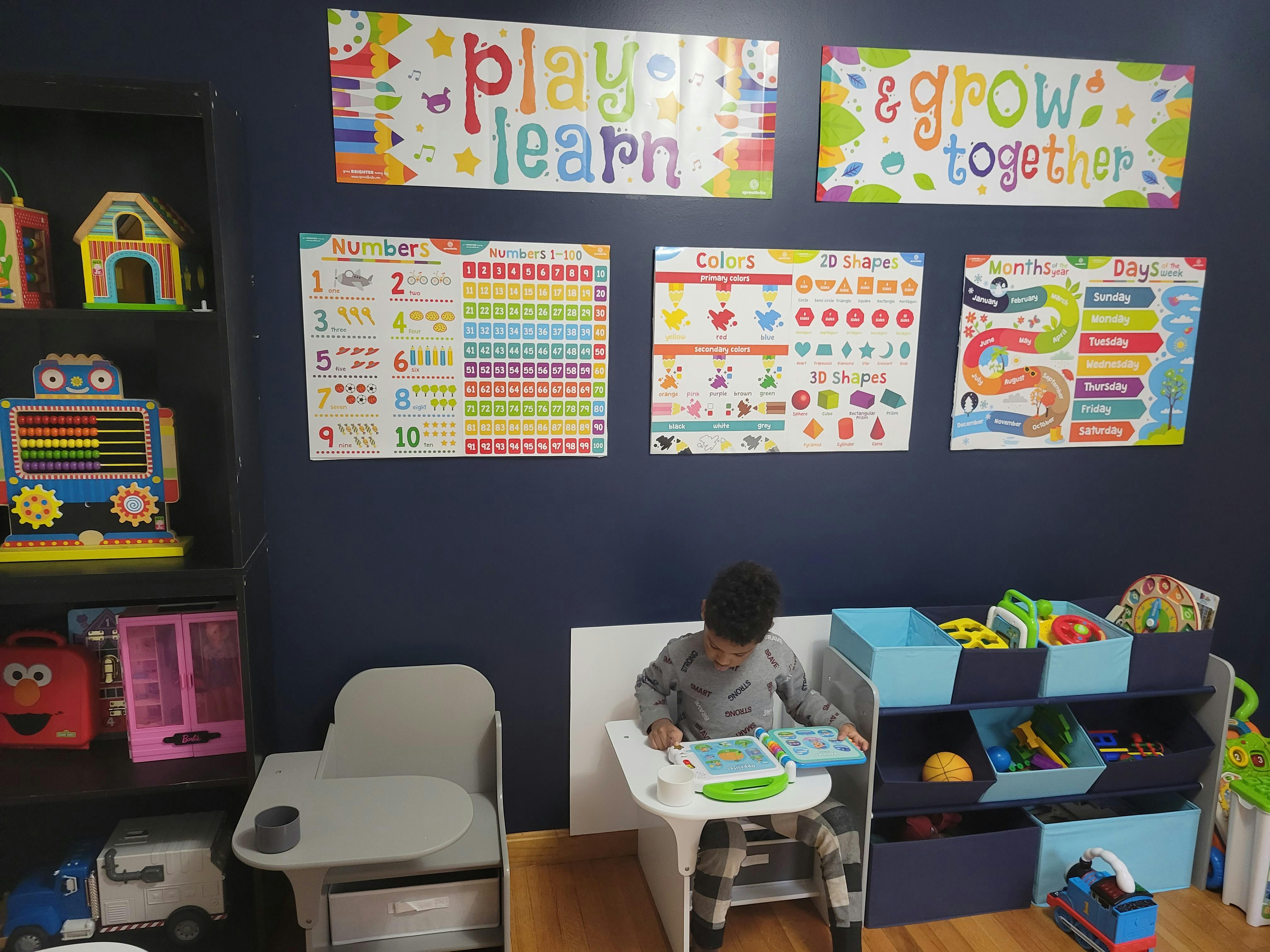 Child sitting at a small desk with a toy, "Play & Learn" sign on the wall