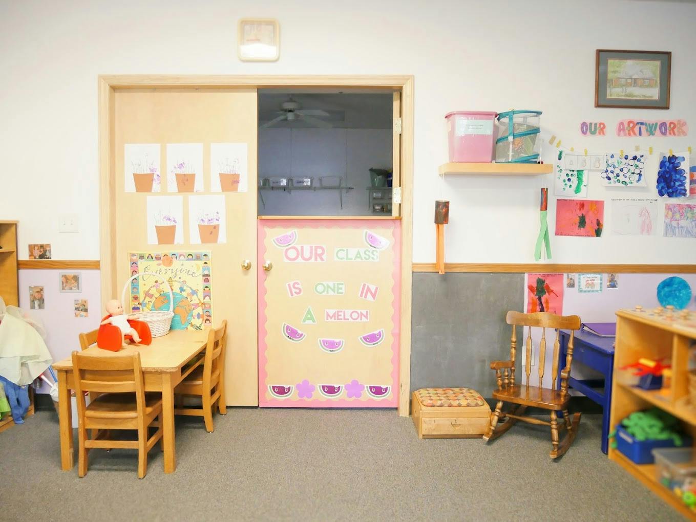 Classroom with small wooden tables and chairs, decorated door, and artwork on walls
