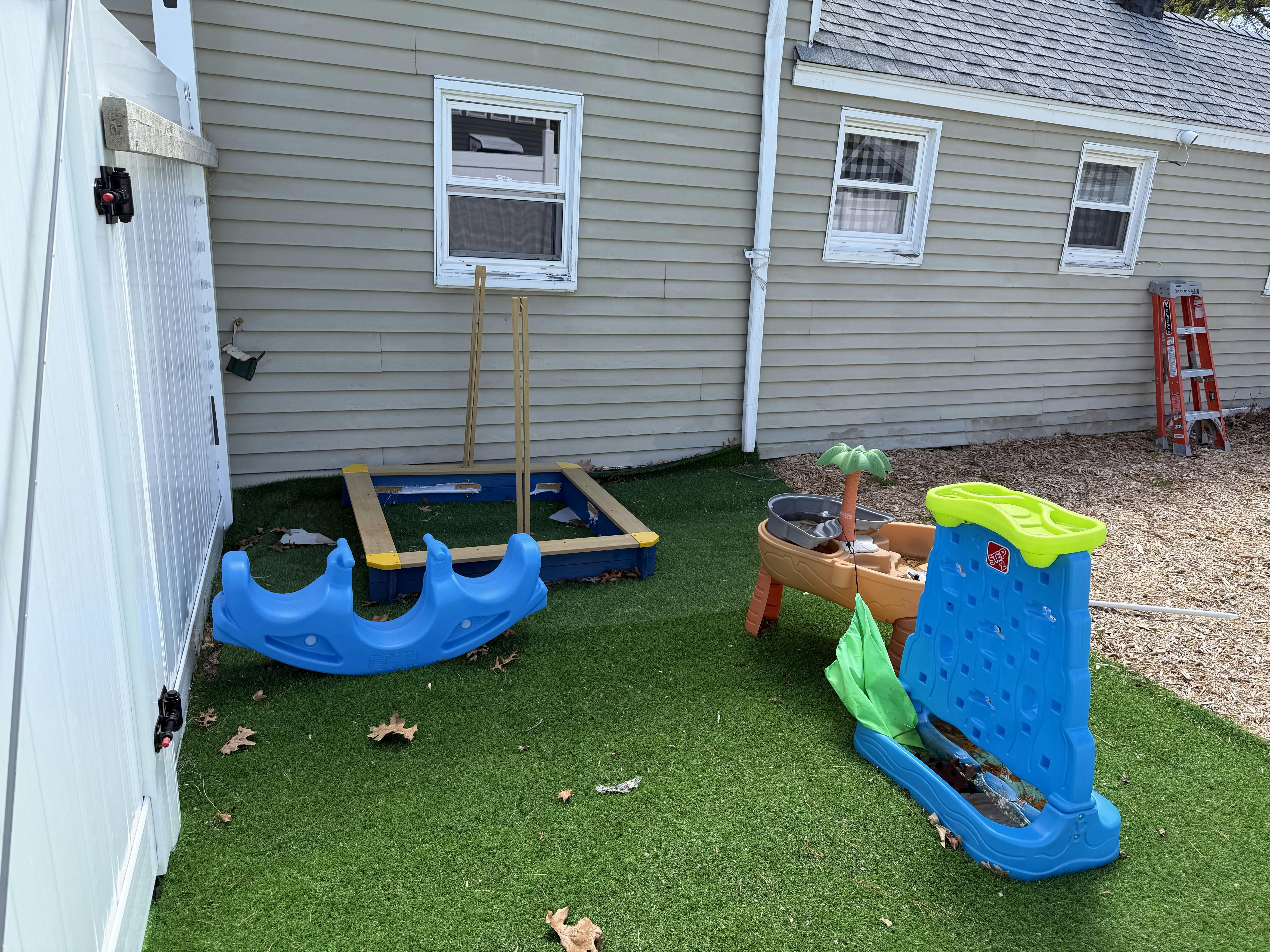 Children's play area with a sandbox, blue rocker, and water table