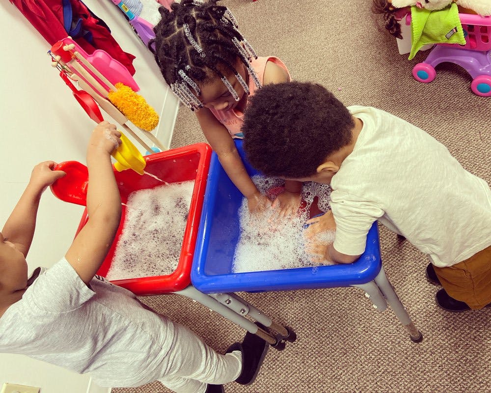 Three children playing with water and bubbles in red and blue bins