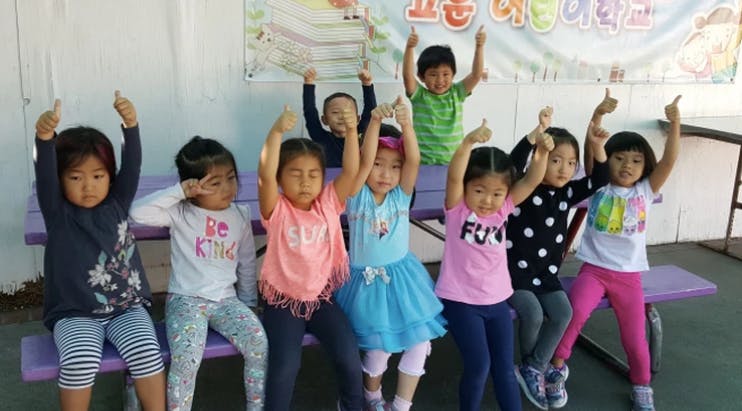 Group of children with arms raised, some sitting on a bench