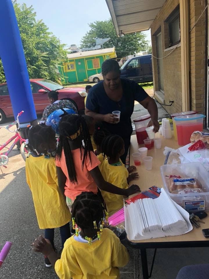 Person pouring drinks for children at a table outdoors