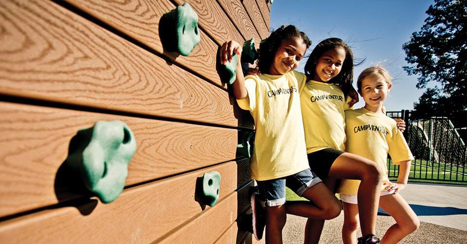 Three children standing next to a climbing wall