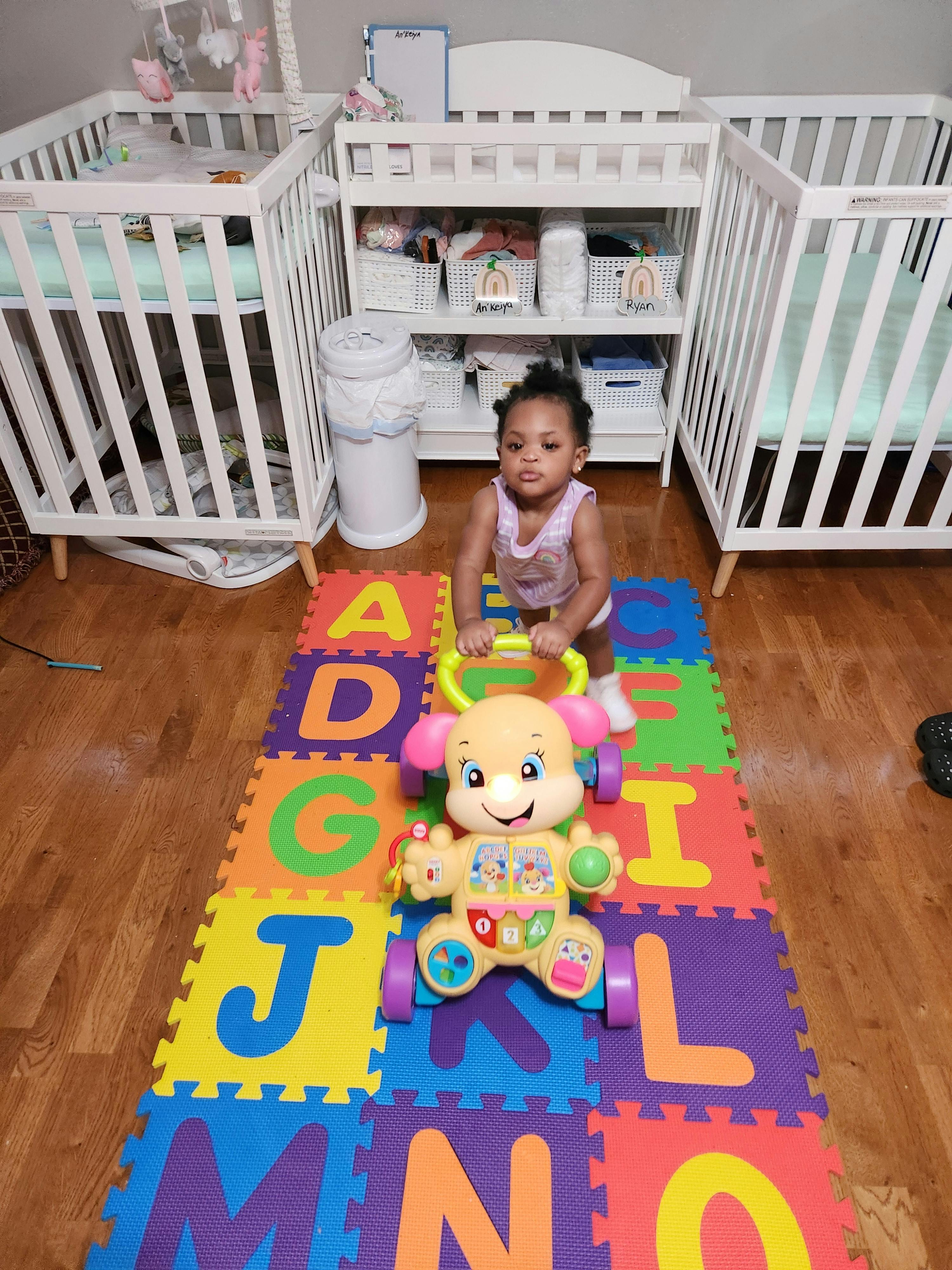 Child standing on alphabet mat with a toy walker