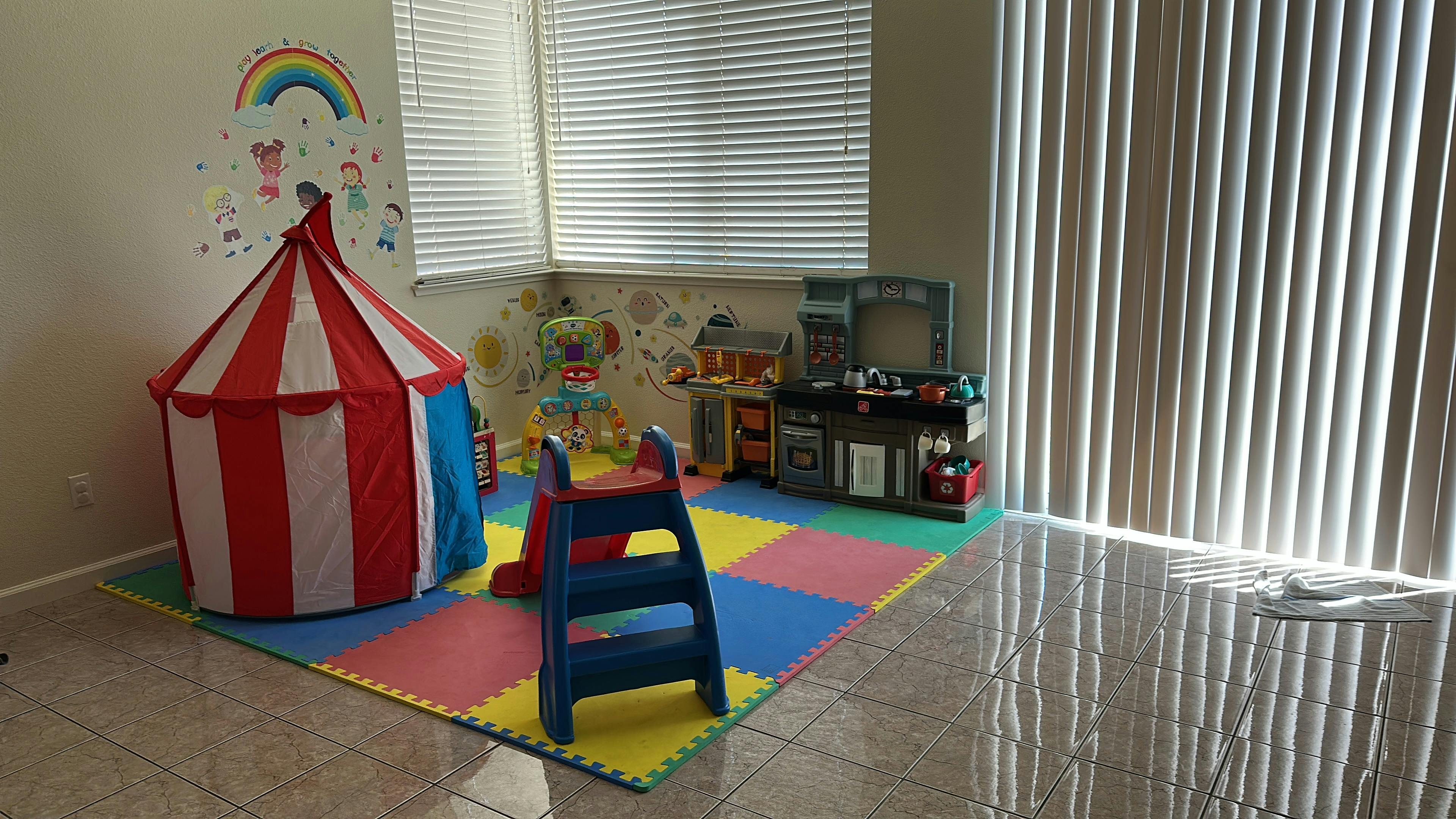 Play area with a toy tent, slide, and pretend kitchen on colorful floor mats