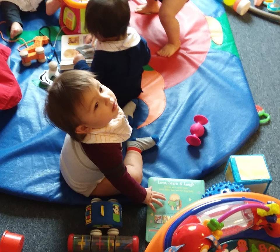 Child sitting on a playmat with toys and another child