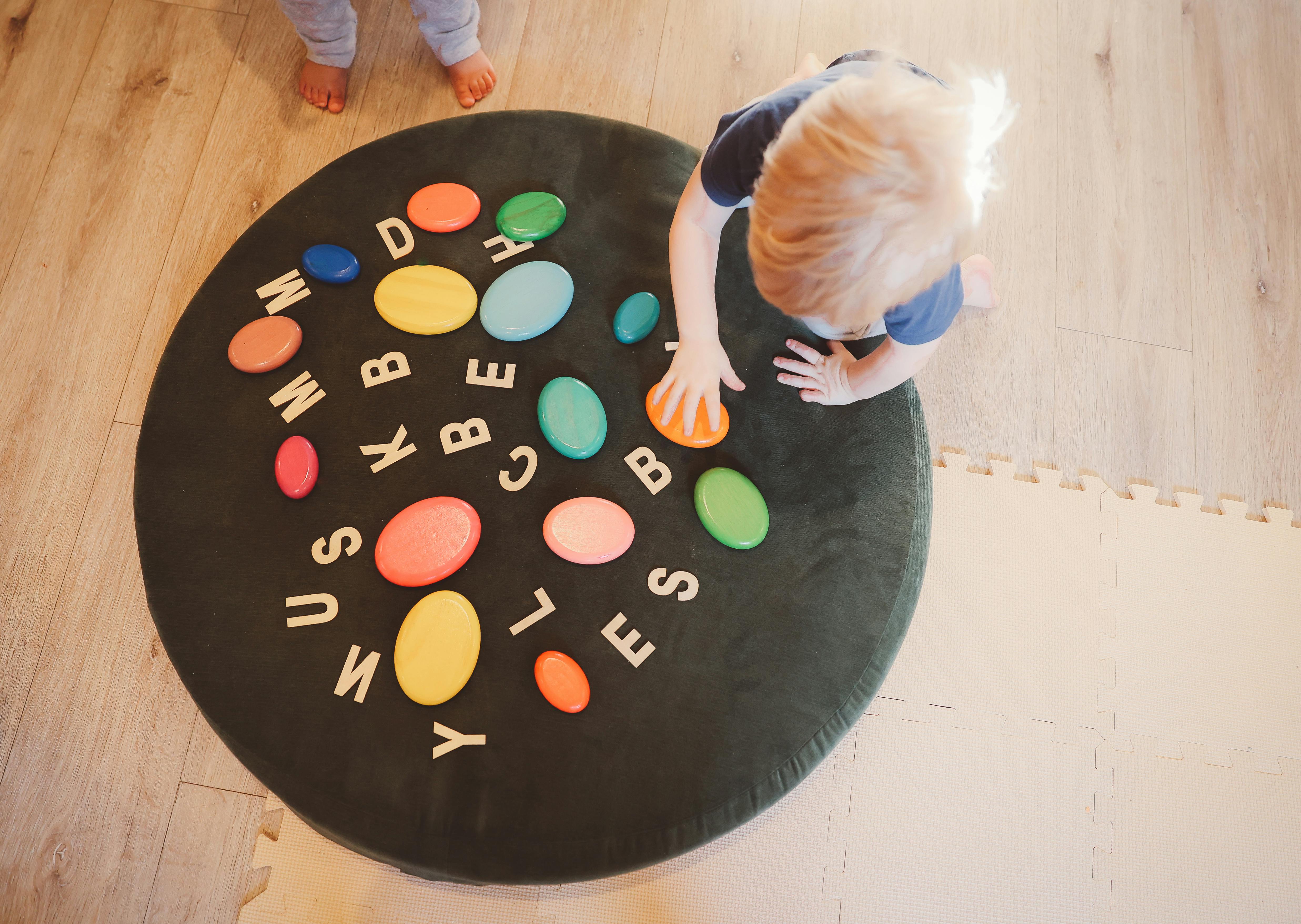 Child playing with colorful letter shapes on a round mat