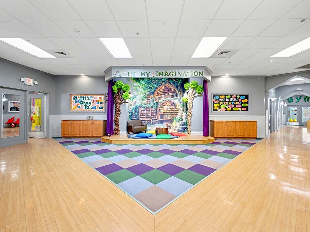 Children's classroom with stage, colorful rug, and text "IN MY IMAGINATION"