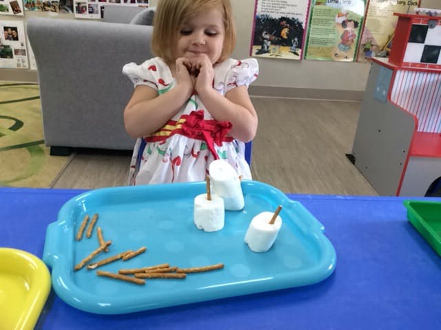 Child looking at marshmallows and pretzel sticks on a blue tray