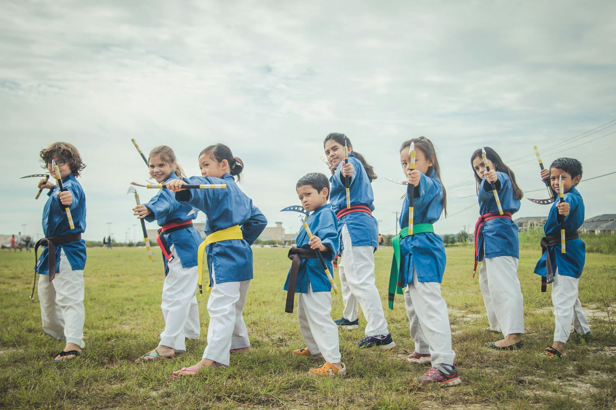 Children in martial arts uniforms holding sticks outdoors