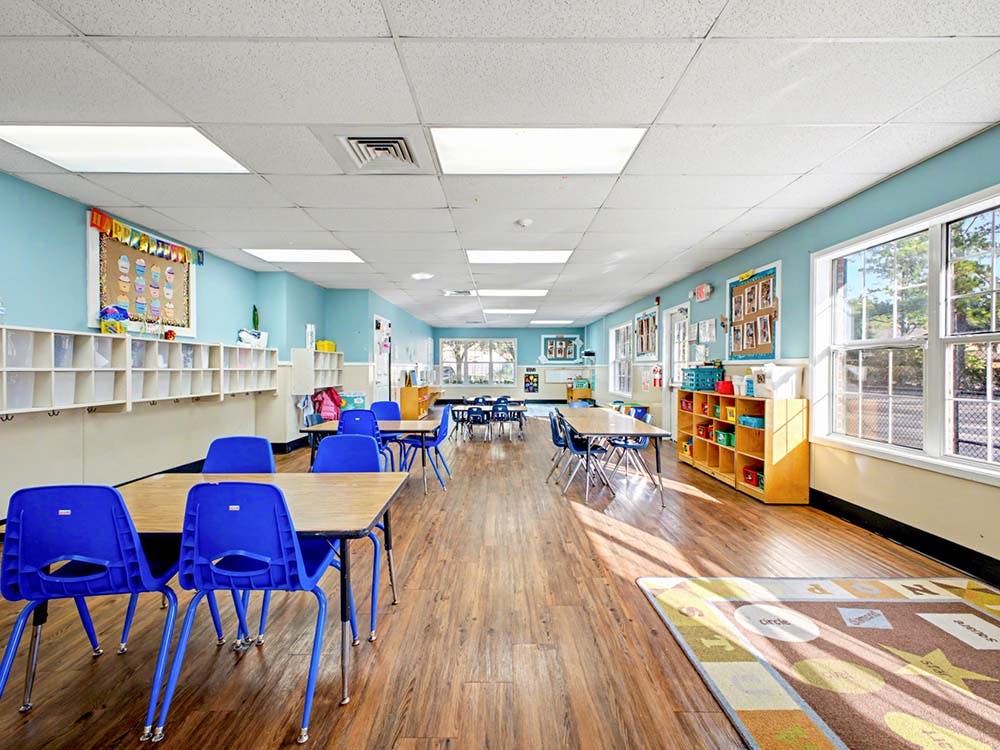 Empty classroom with blue walls, wooden floors, tables, and blue chairs