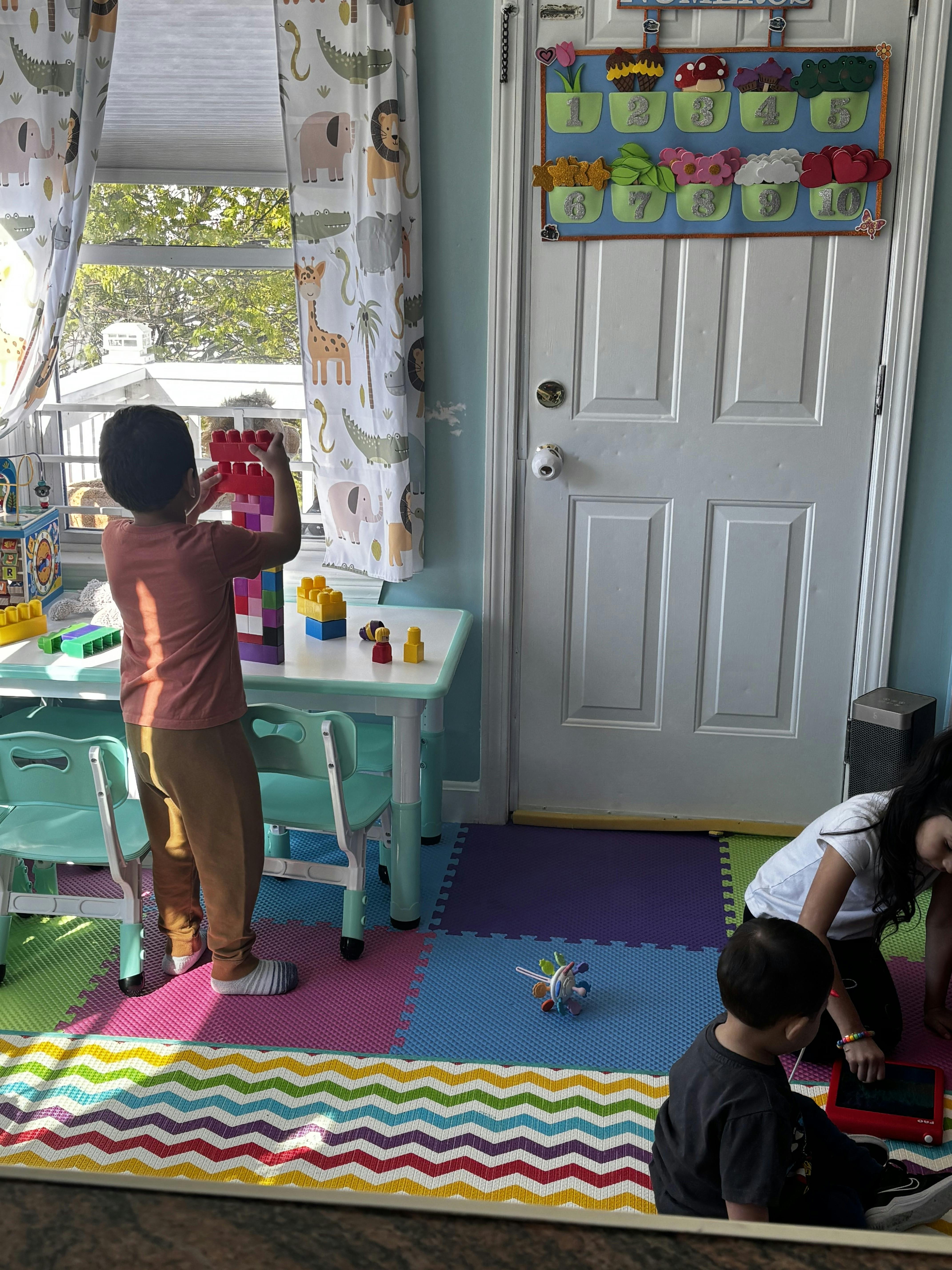 Child standing, building a tower with colorful blocks on a table with other children
