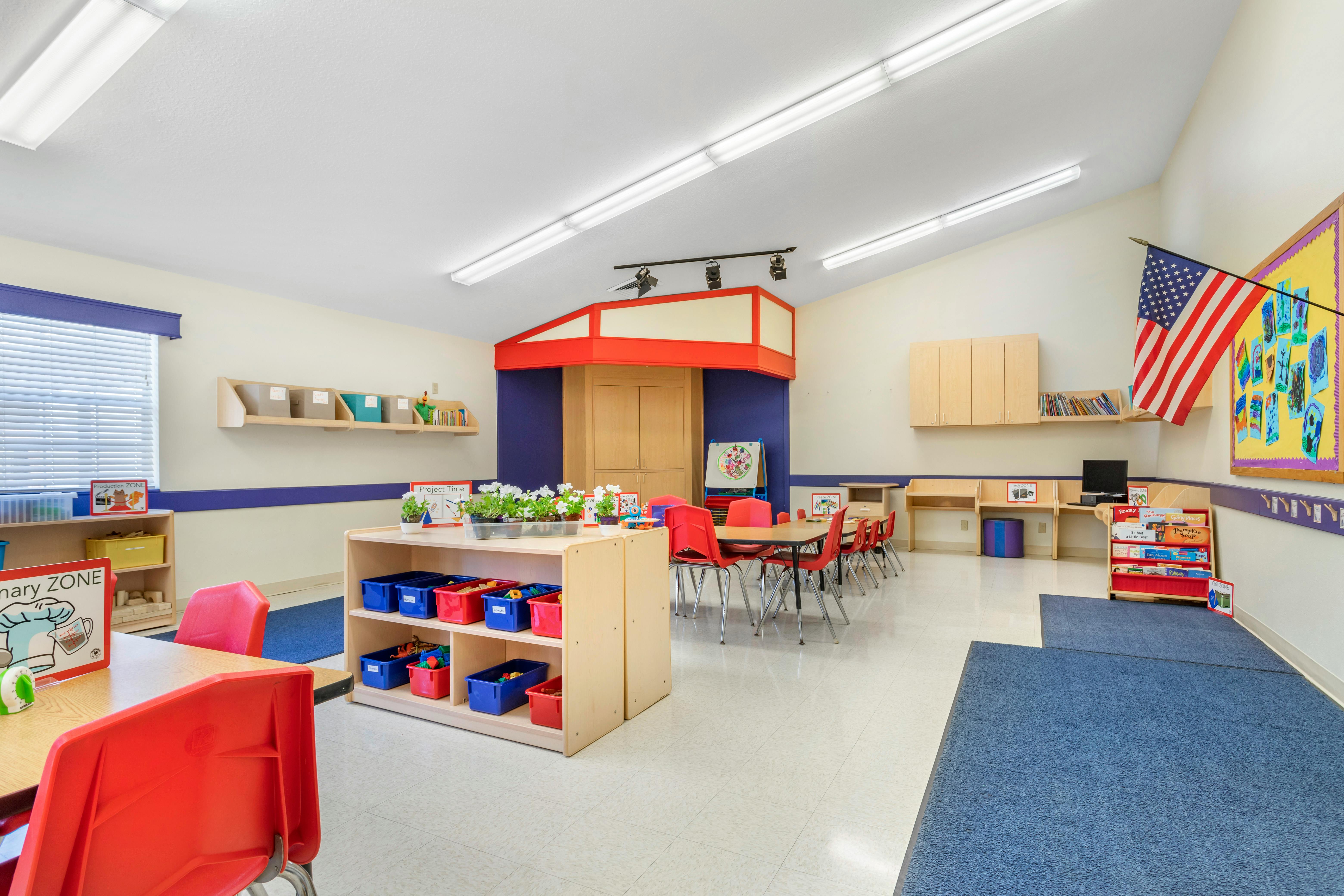 Classroom with small tables, red chairs, bookshelves, and various learning zones