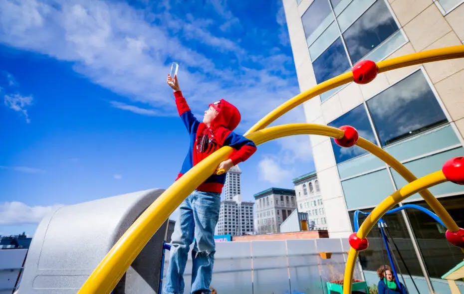 Child in a red and blue hoodie holding up a clear bottle on a playground