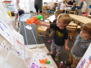 Child spraying paint onto a canvas with a toy water gun