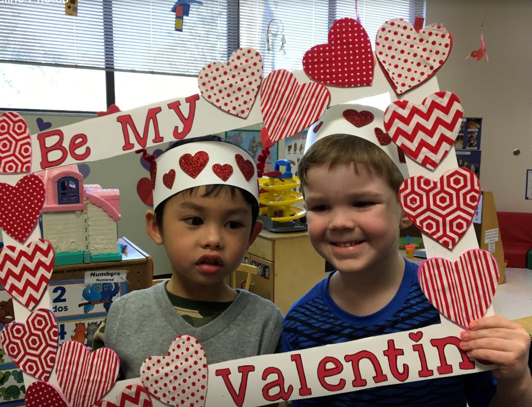 Two children wearing heart crowns and holding a "Be My Valentine" sign