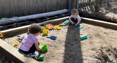 Two children playing in a sandbox with toys