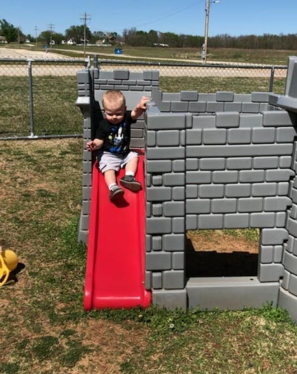 Child on a red slide attached to a gray play structure