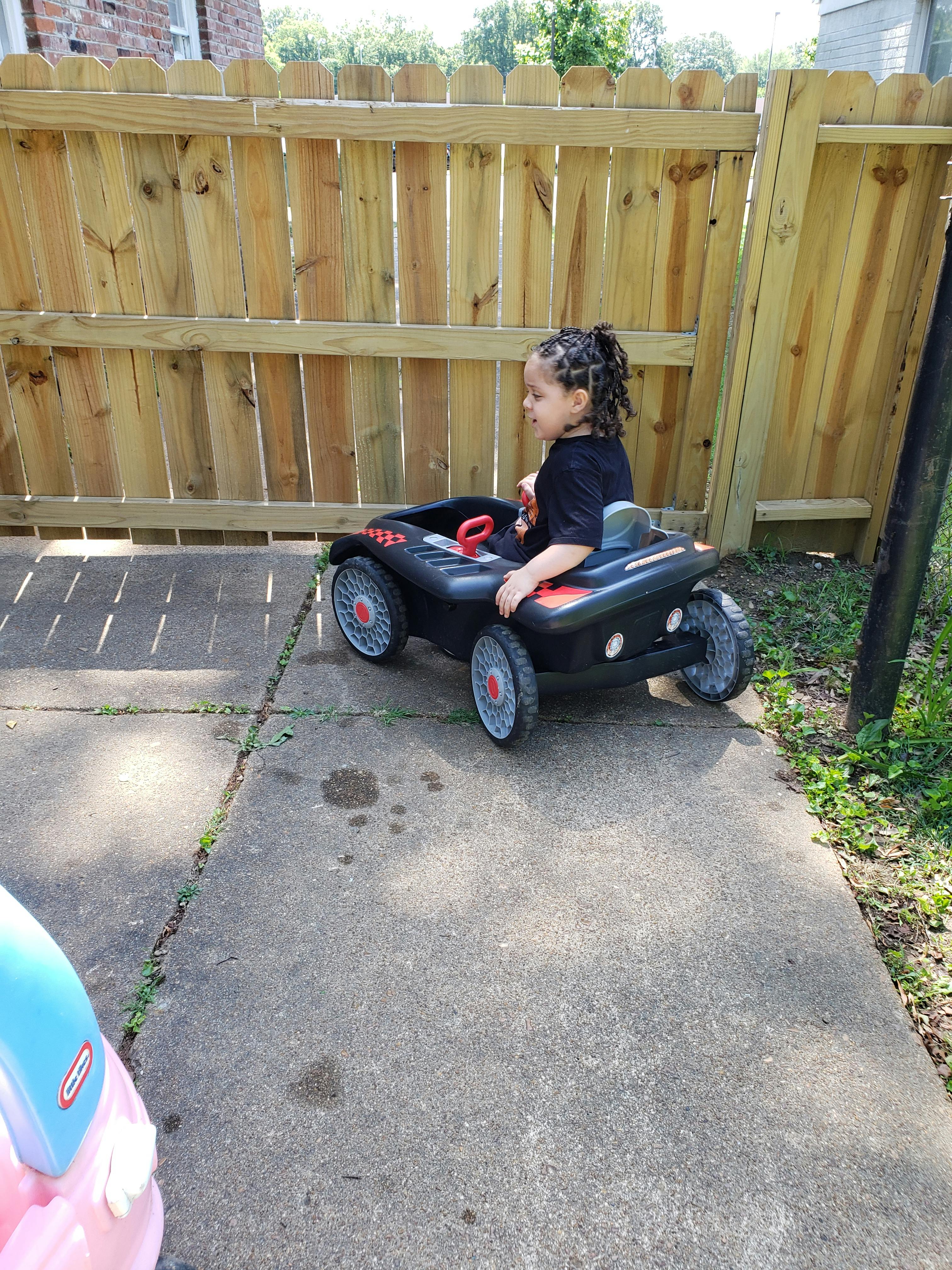 Child sitting in a toy car on a concrete path