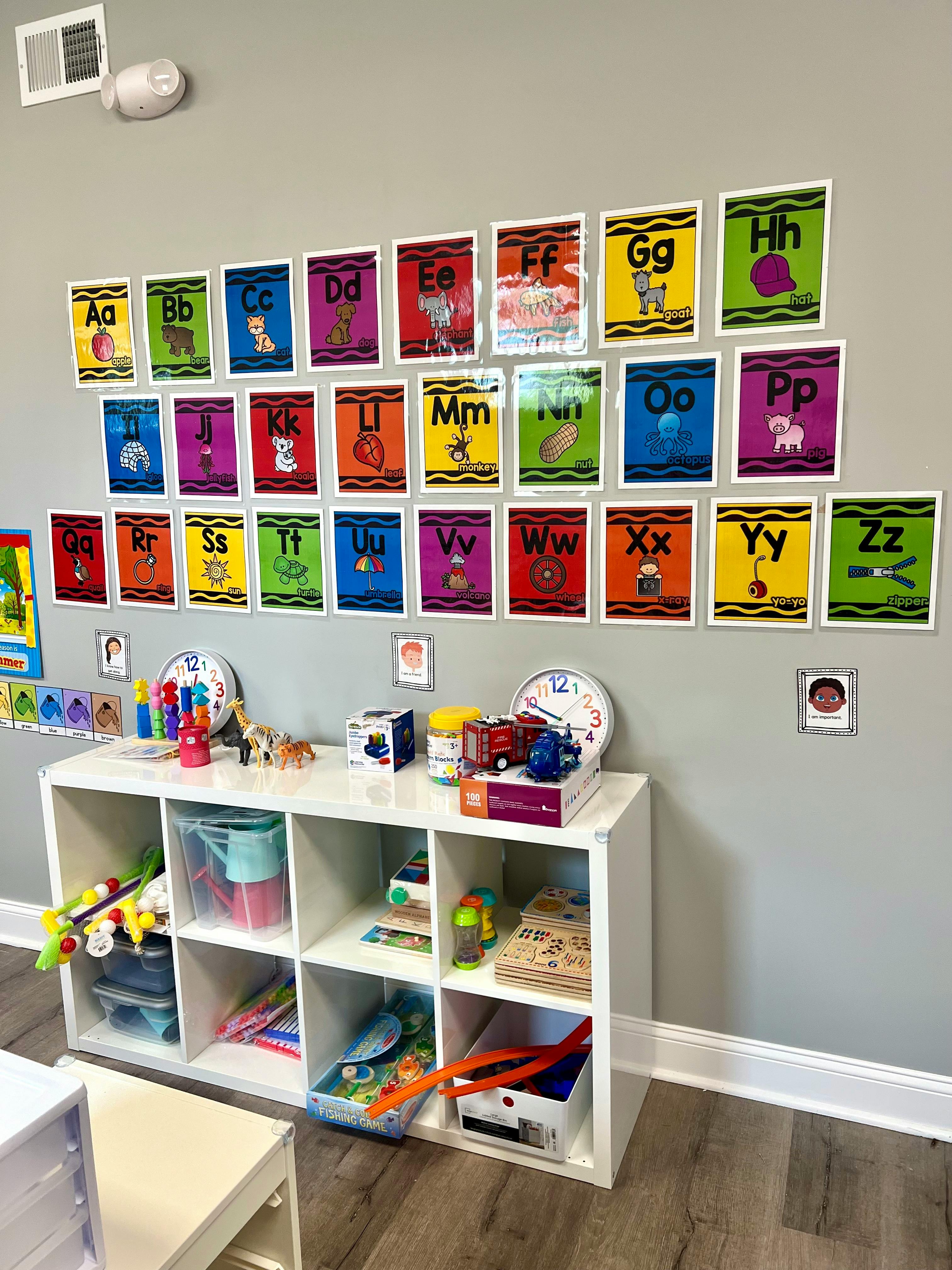 Alphabet cards on a wall above a white storage shelf with toys