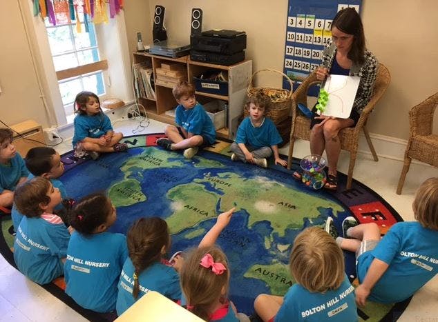 Adult reading to children sitting on a world map rug in a classroom