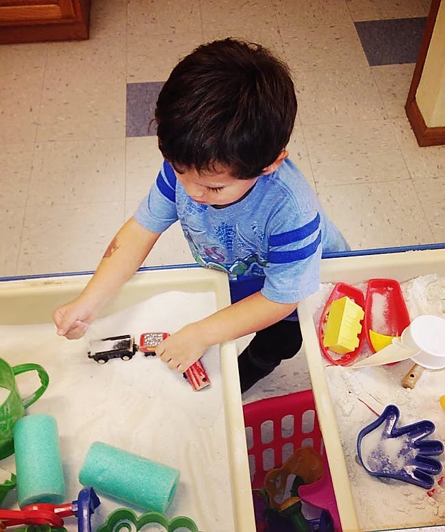 Child playing with toy trains in a sand table