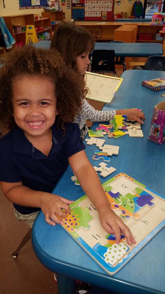 Child smiling while playing with a puzzle in a classroom