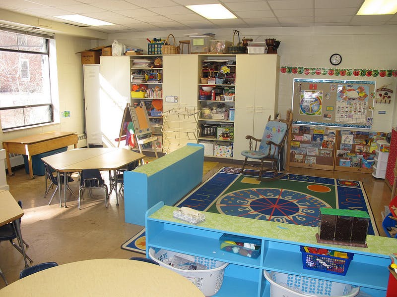 Classroom with tables, chairs, storage shelves, and a colorful rug