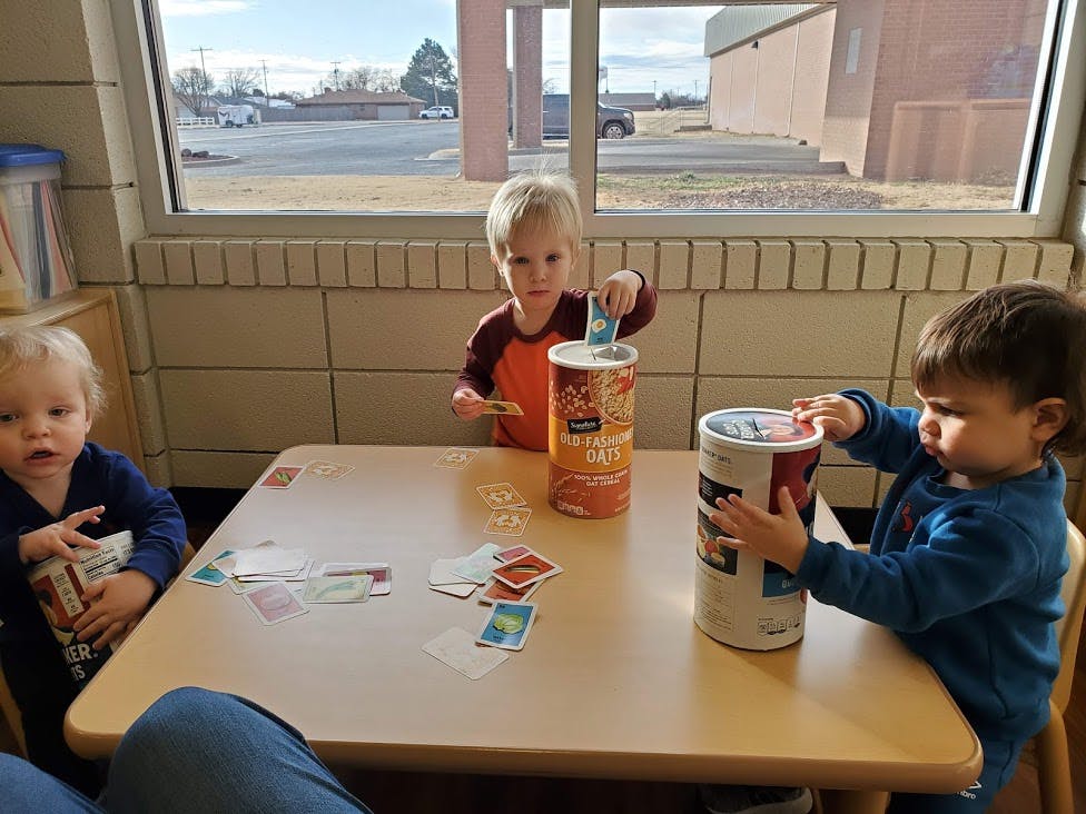 Three children at a table playing with cards and containers