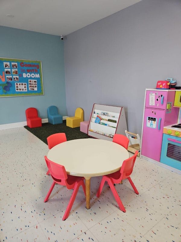 Classroom with a round table and chairs, colorful chairs on a rug, and play kitchen