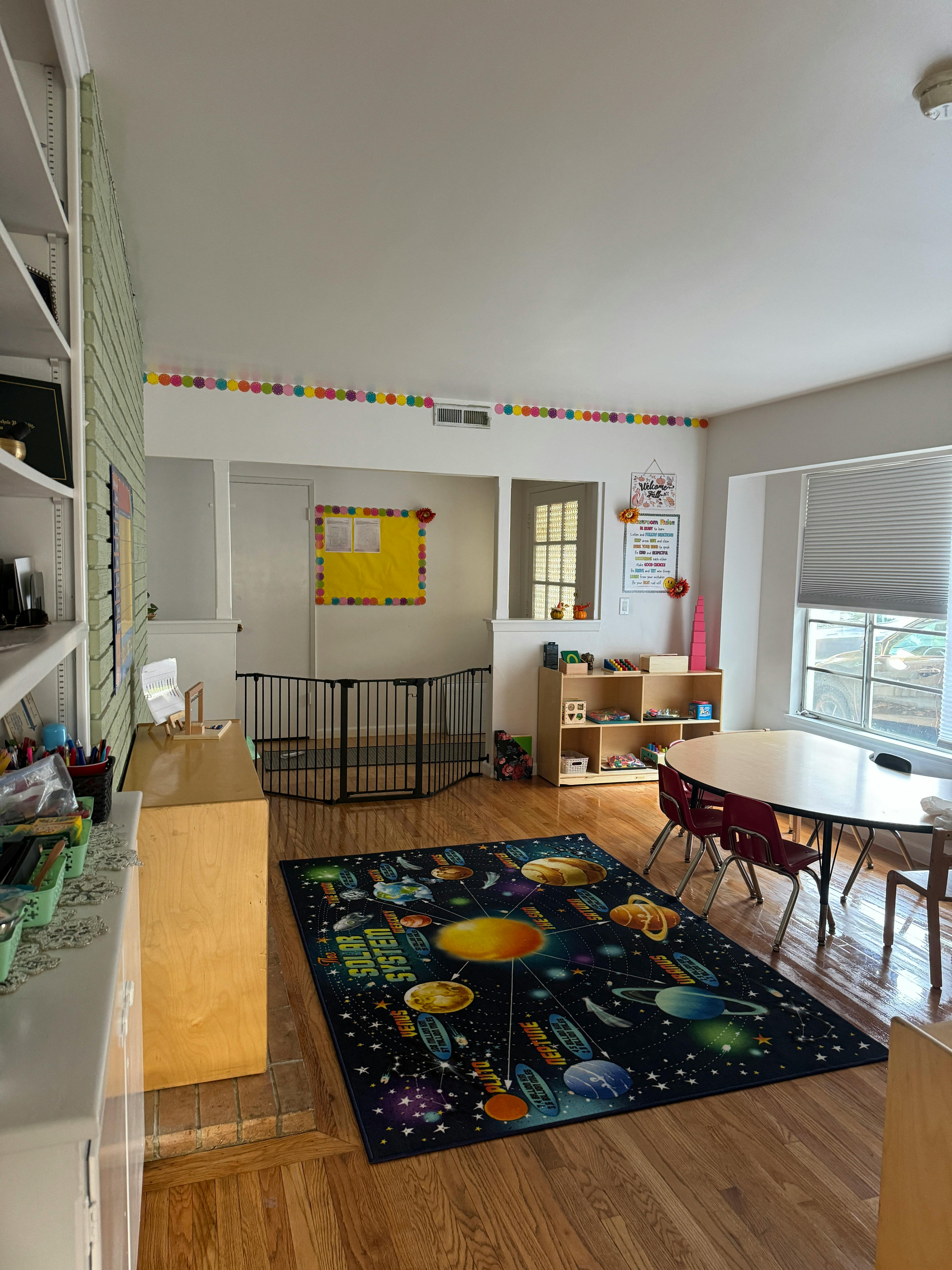 Classroom with a solar system rug, small table and chairs, and baby gate