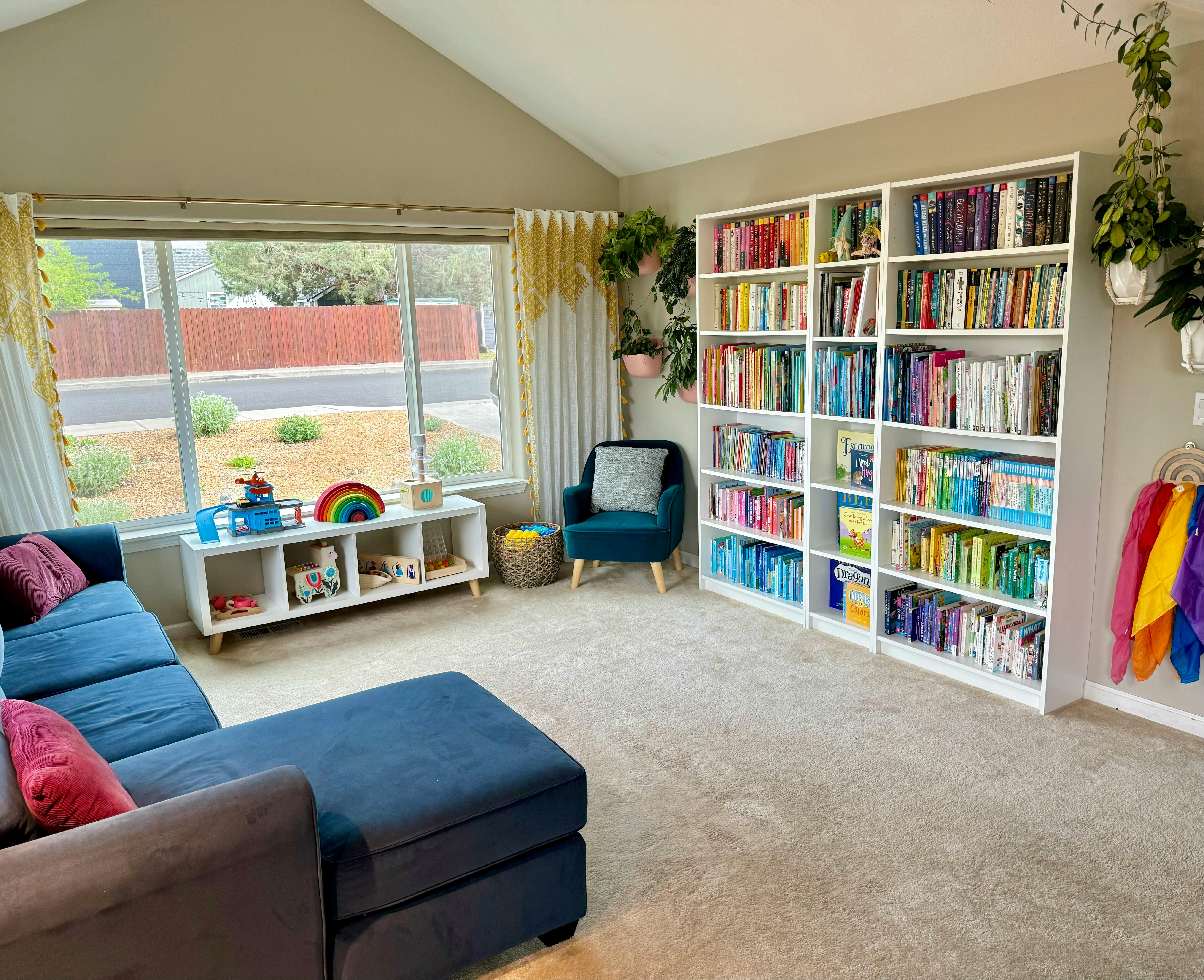 Living room with a blue sectional sofa, large window, and white bookshelves