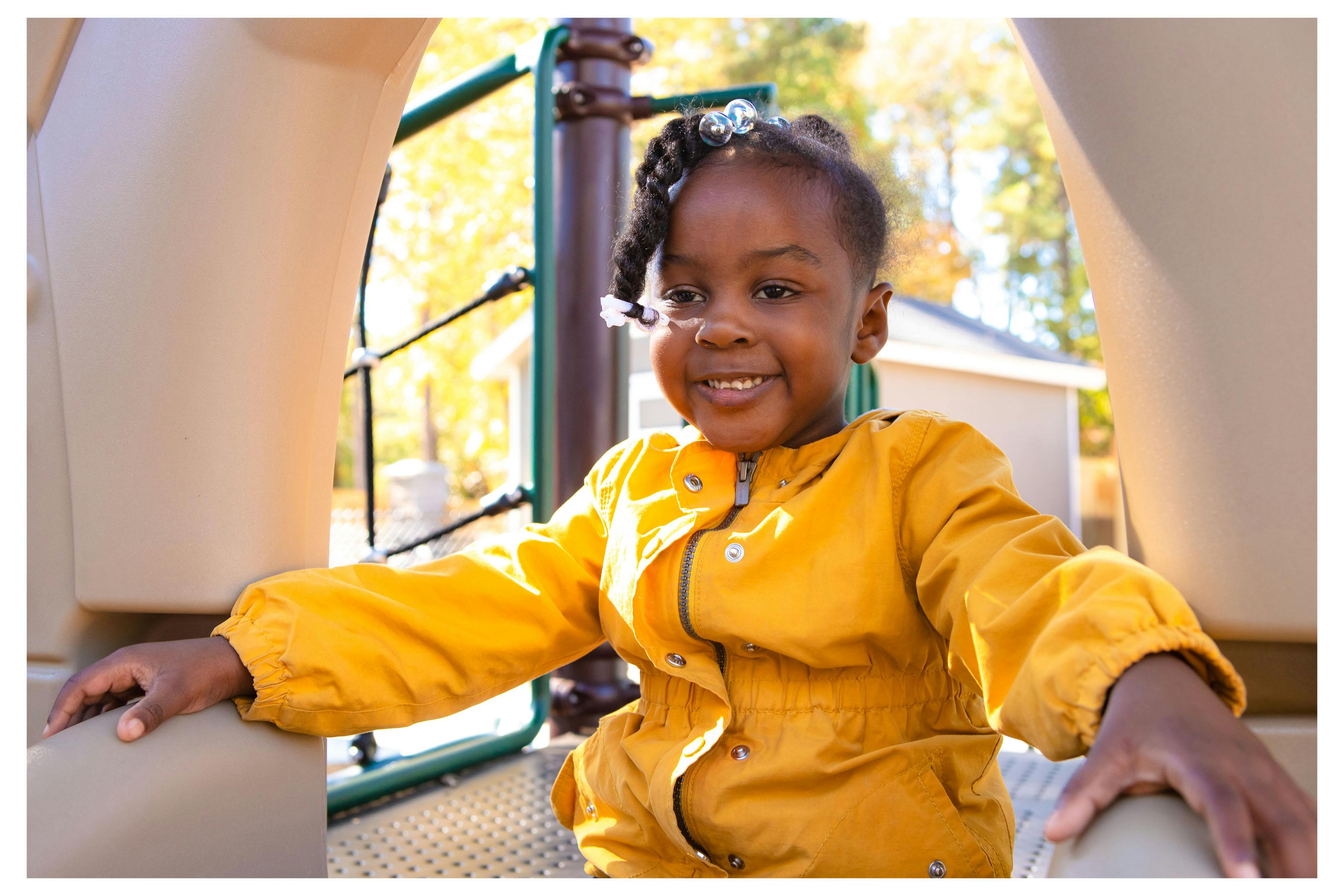 Child in a yellow jacket on a playground structure at a playground