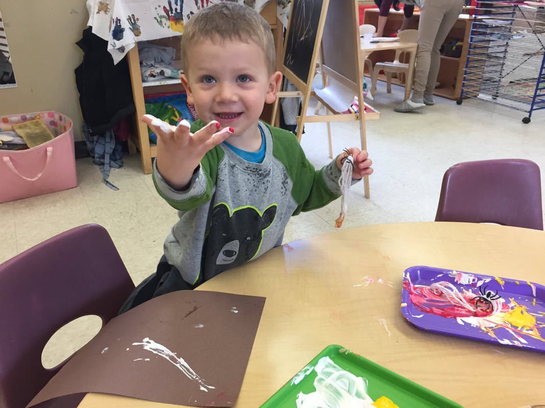 Child at a table with paint on hands and paper