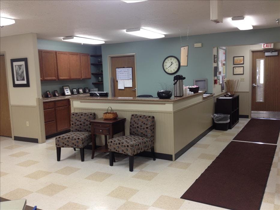 An empty reception area with a counter, chairs, and an exit door
