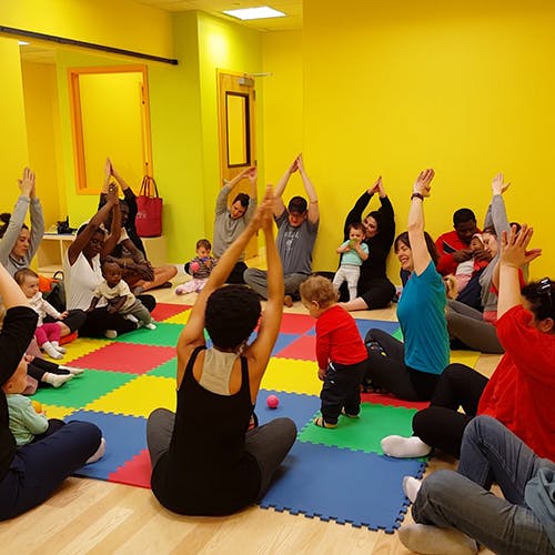 Adults and children sitting on a colorful mat with arms raised
