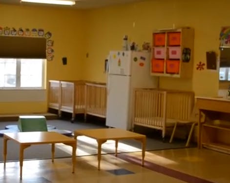 Daycare room with cribs, small tables, and a refrigerator