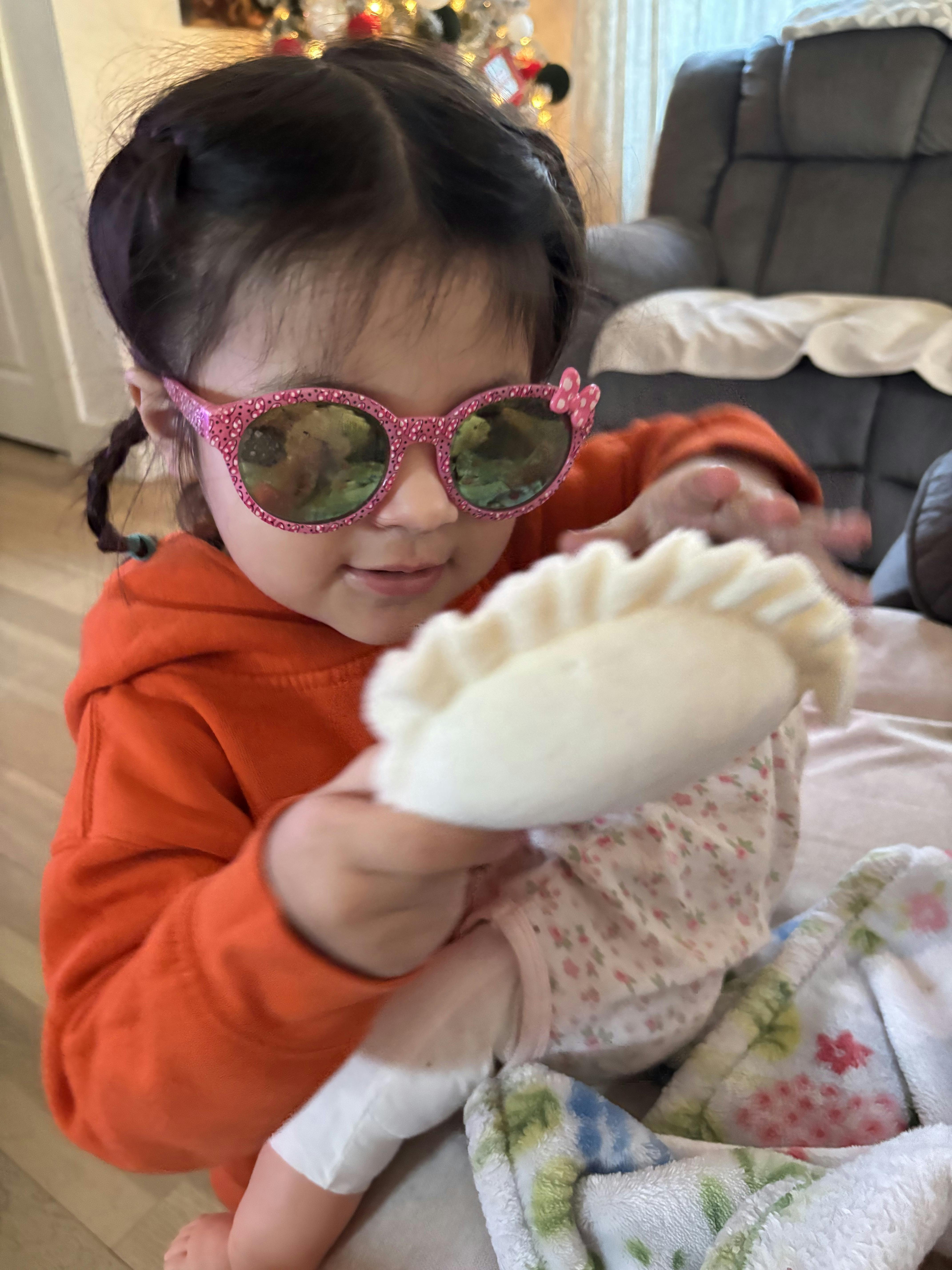 Child wearing pink sunglasses and an orange hoodie holding a doll