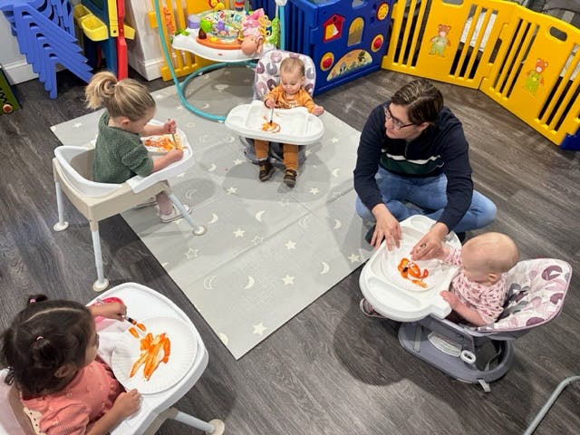 Person with three children in high chairs eating