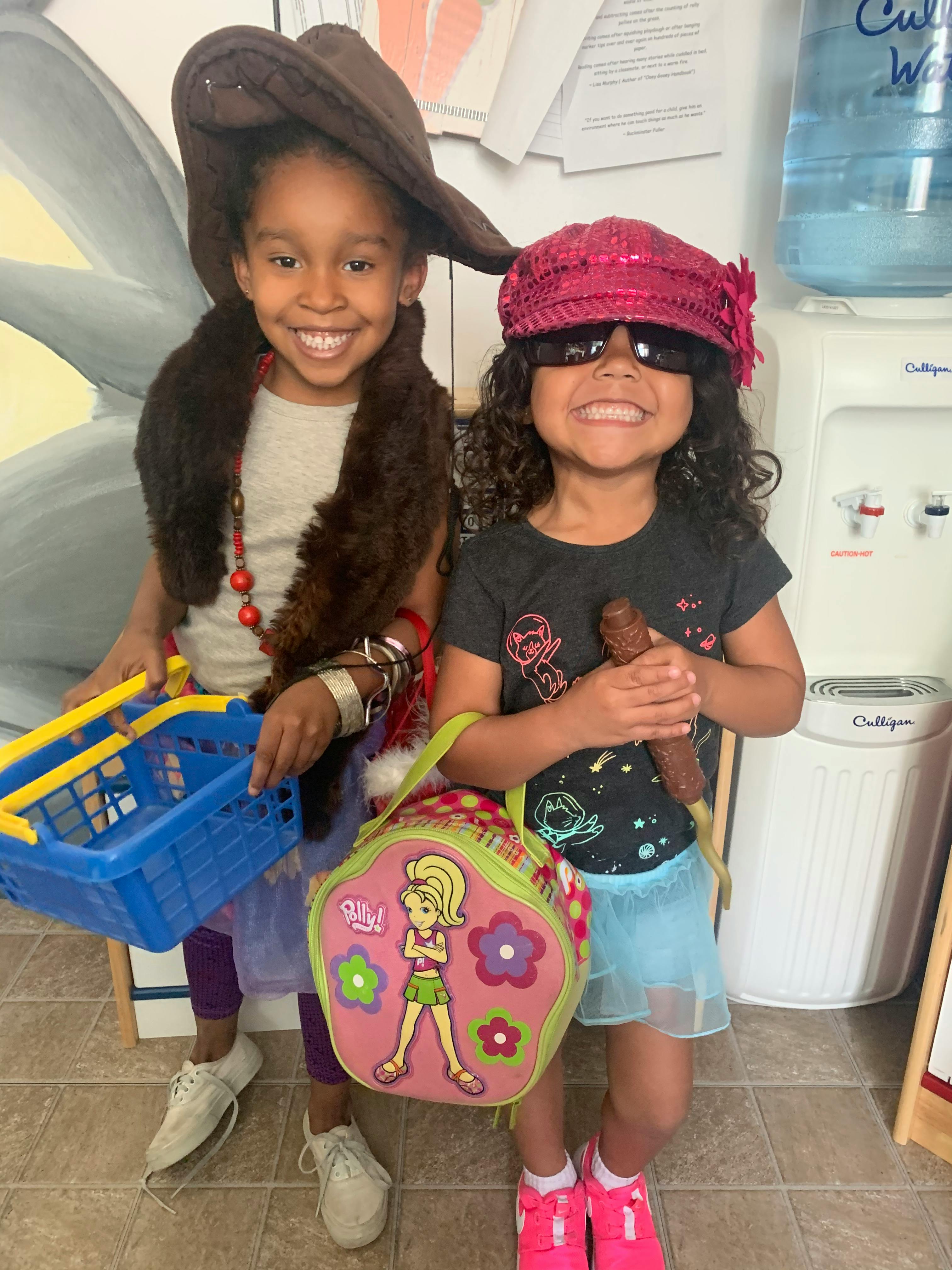 Two children in costumes holding a shopping basket and a bag