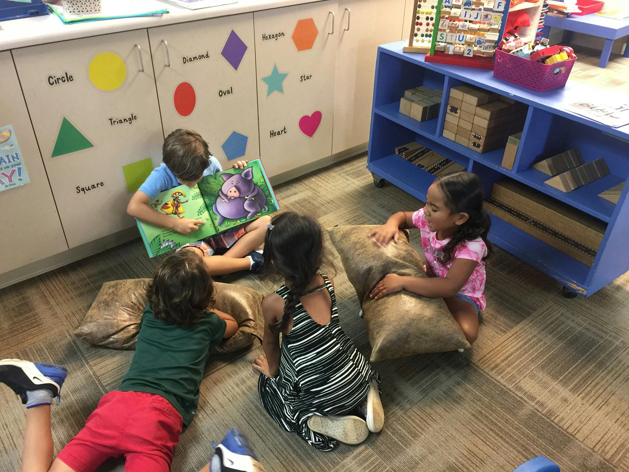 Children sitting on floor cushions reading a book in a classroom