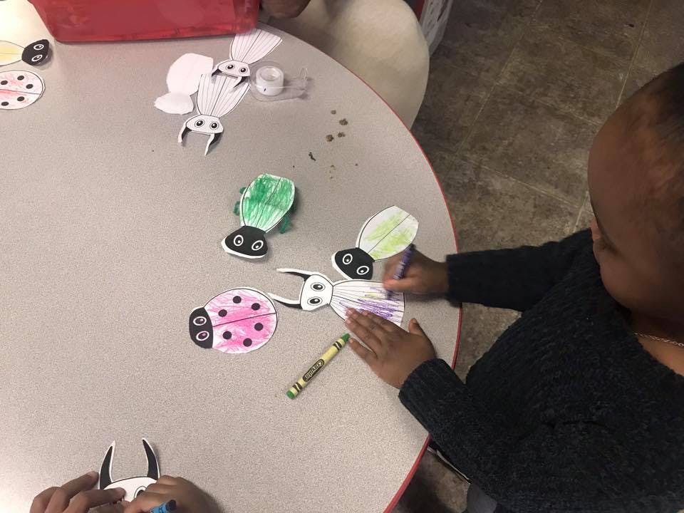 Child coloring paper cutouts of insects at a table