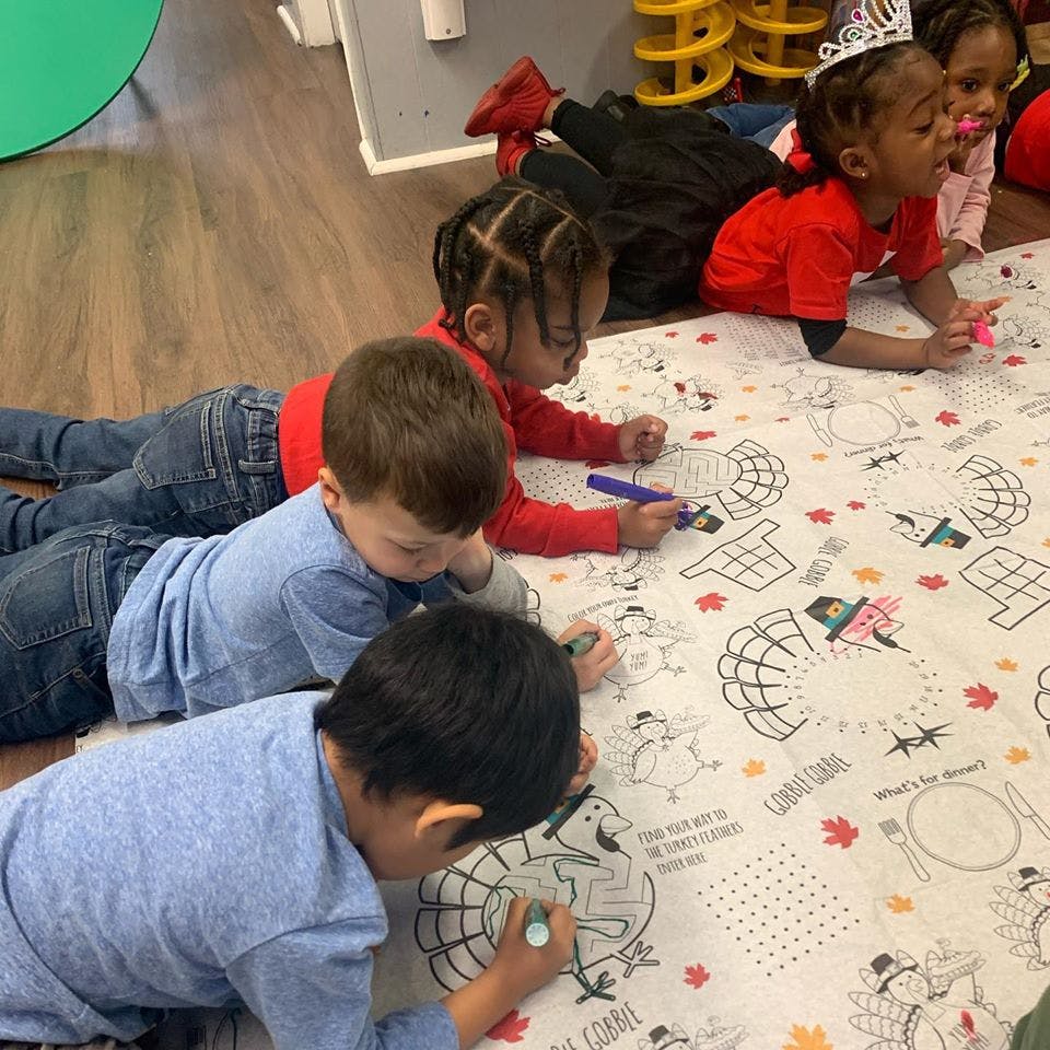 Children lying on the floor coloring a large sheet of paper