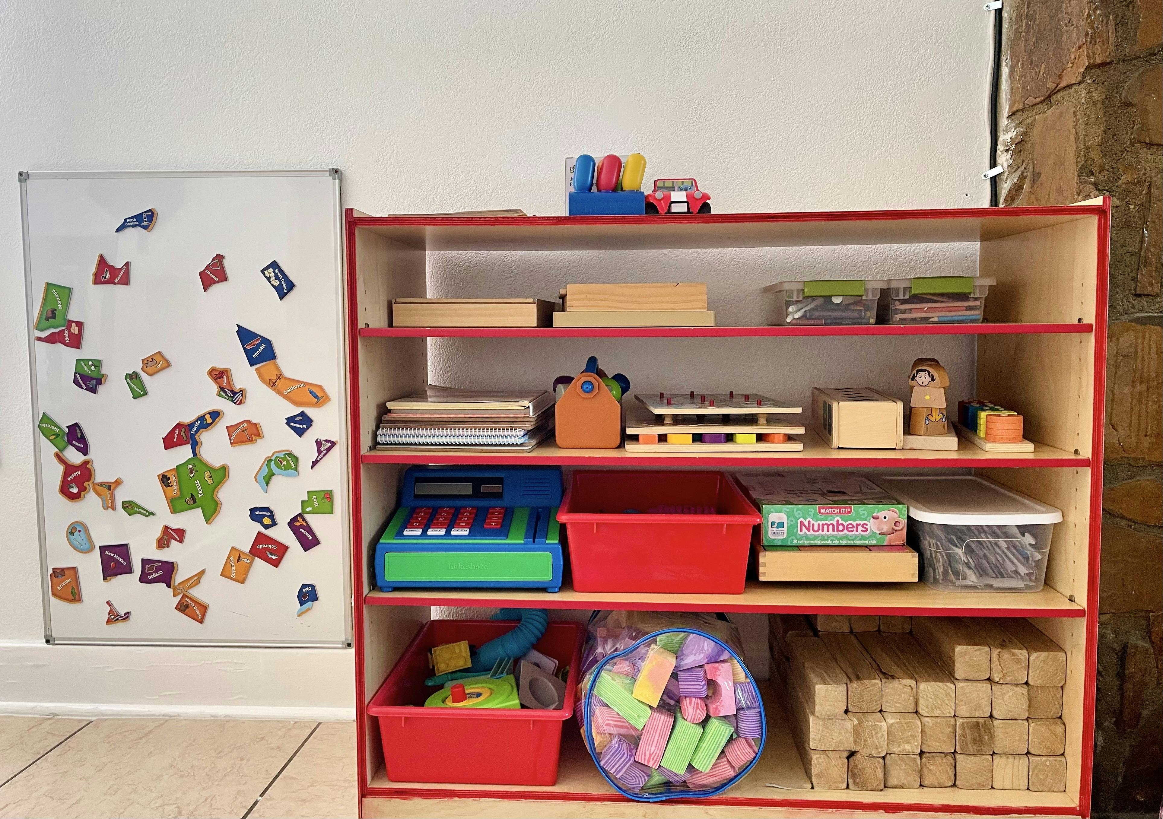 Shelf with toys and learning materials next to a whiteboard with magnets