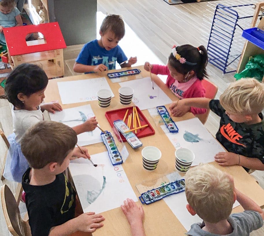 Children painting at a table in a classroom