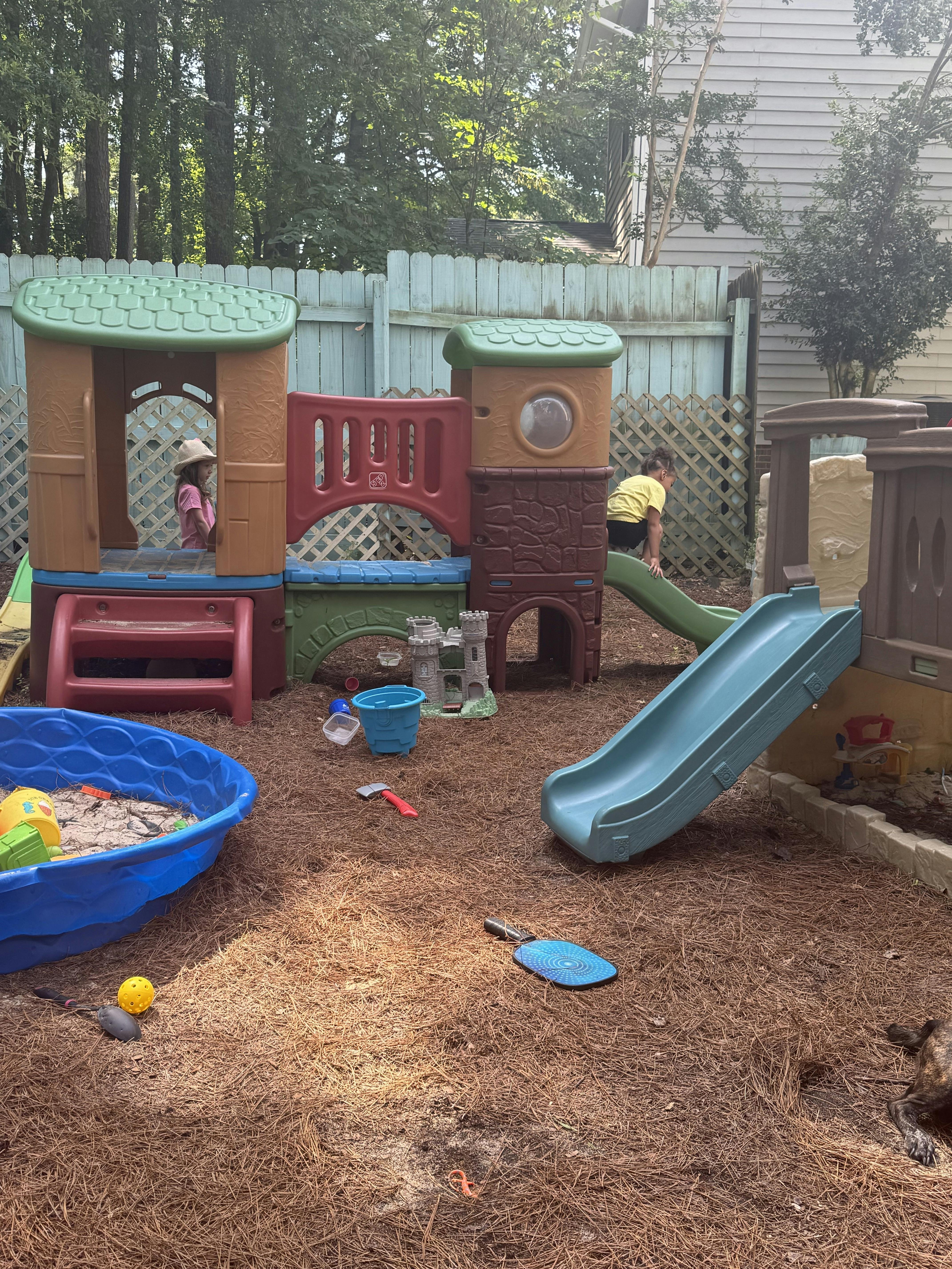 Two children playing on a backyard playground with slides and a sandbox