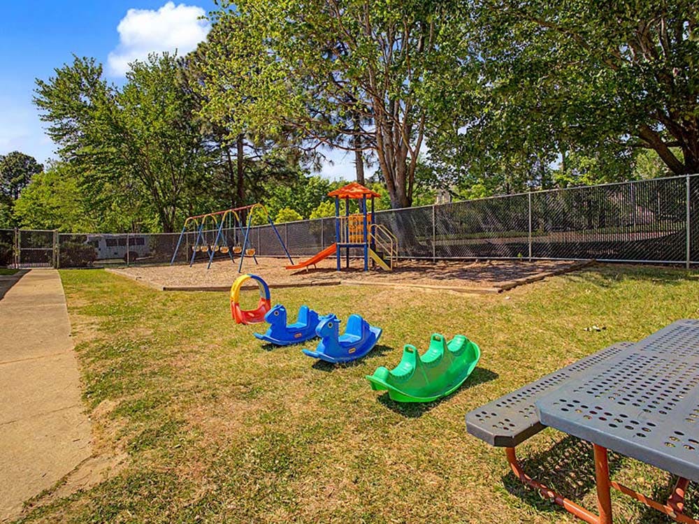 Playground with swings, a slide, and spring riders on grass next to a picnic table