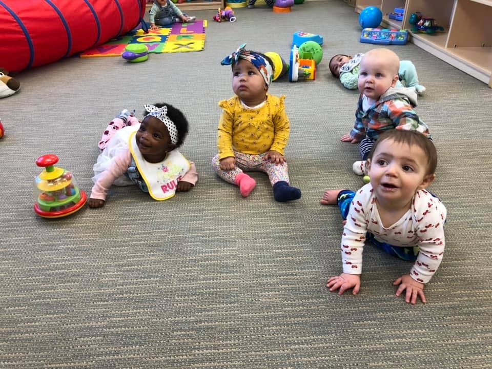Multiple babies on a carpeted floor with toys