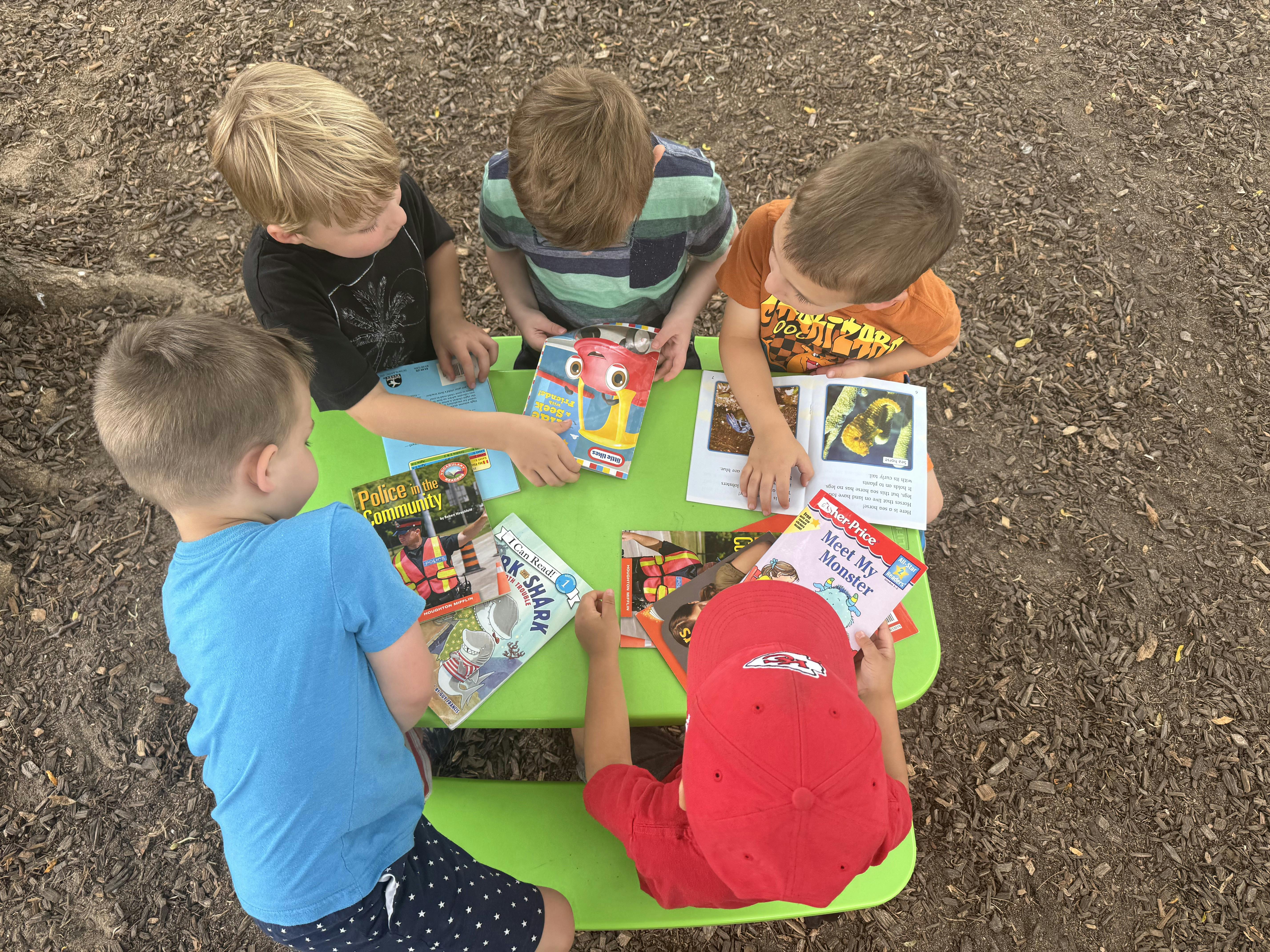 Five children sitting at a small table reading books together